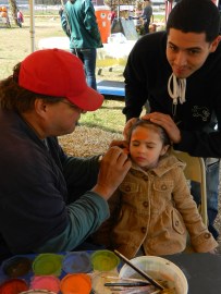 Fernando of Manchester holds his daughter Makayla's hair out of her face as Kevin Sterling paints on a pumpkin. 