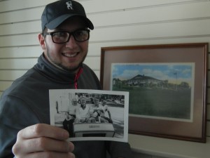 Patrick Kozelka holds a photo of his grandfather, Milton Kozelka, Sr. who served as club president circa the 1960s - he is shown at the wheel of the golf cart. In the background is a painting of the golf club.